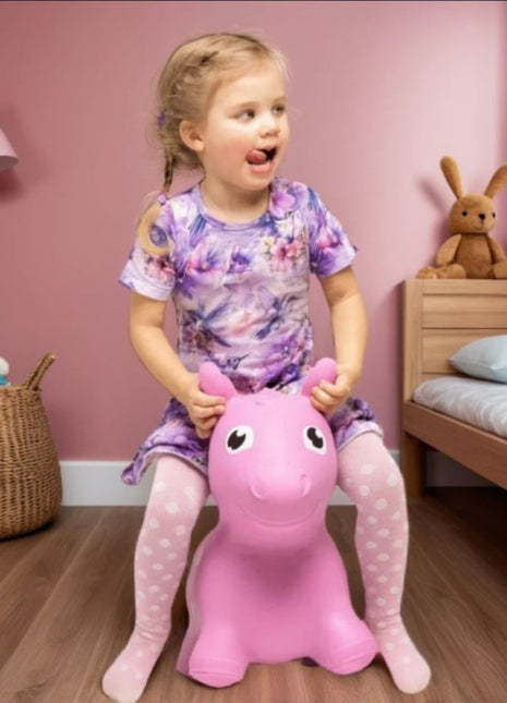 Kind zit op My First Jumpy roze springpaard in roze slaapkamer.