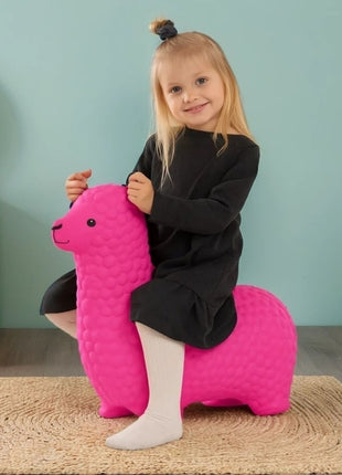 Meisje zit op roze My First Jumpy springalpaca op jute kleed voor blauwe muur.