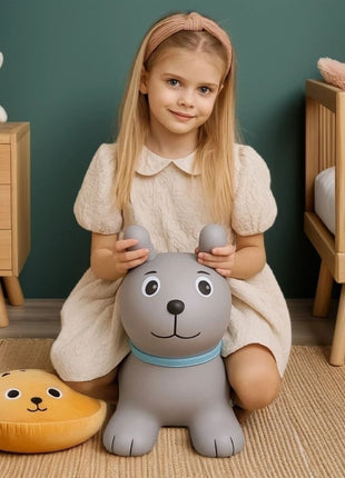 Meisje zit op grijze My First Jumpy springhond op vloerkleed voor groene muur.