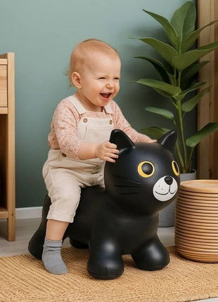 Lachende peuter zit op zwarte My First Jumpy springkat in speelhoek met planten.