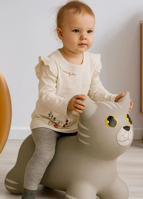 Peuter zit op grijze My First Jumpy springkat op licht vloerkleed in kinderslaapkamer.