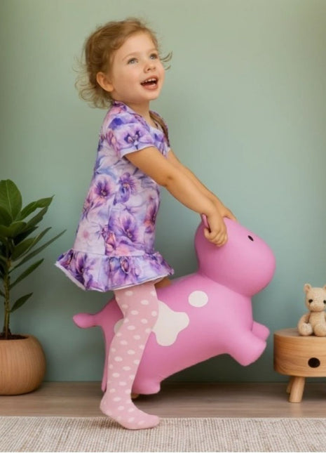 Meisje duwt op roze My First Jumpy springkoe naast planten en speelgoed.