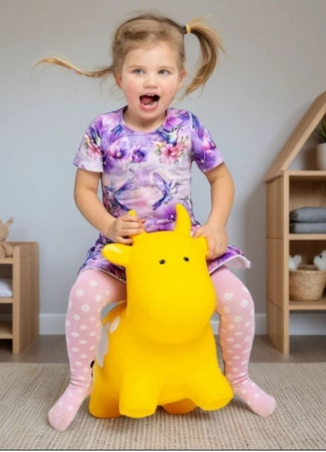 Meisje rijdt op gele My First Jumpy springkoe in speelkamer met houten meubels.