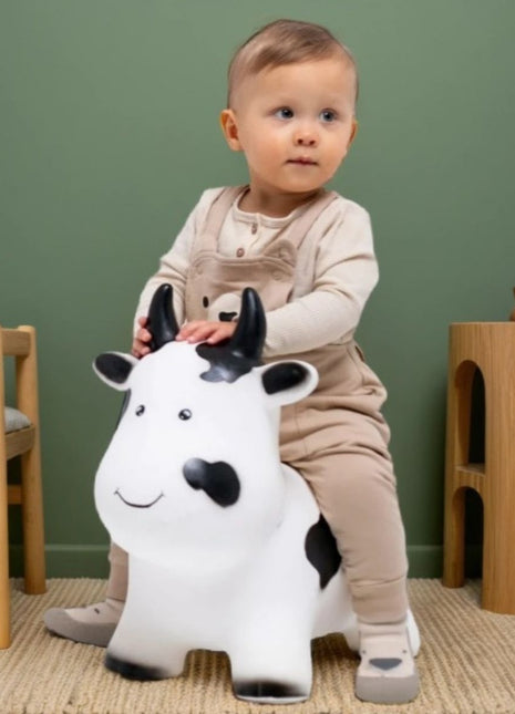 Kind zit op My First Jumpy wit-zwarte springkoe in speelkamer met groene muur en houten meubels.