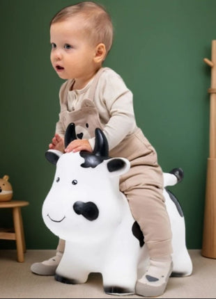 Kind rijdt op My First Jumpy wit-zwarte springkoe, zijaanzicht in kamer met groene muur en houten meubels.