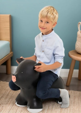 Jongen zit op My First Jumpy zwart varken met bank en mand op de achtergrond.