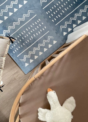 Bovenaanzicht van de OLYA KIDS Boho Azure speelmat in kinderkamer naast wieg en stoel.