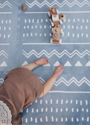 Baby ligt op de OLYA KIDS Boho Azure speelmat met houten speelgoedtrein.