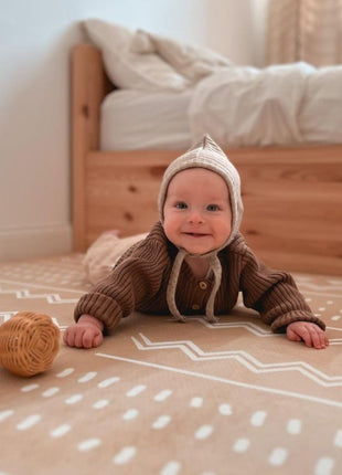 Baby ligt op de OLYA KIDS Boho Zand speelmat met gevlochten speelgoed in slaapkamer.