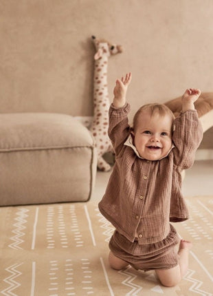 Baby zit met armen omhoog op de OLYA KIDS Boho Zand speelmat in neutrale kamer.