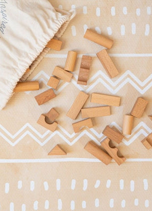 Houten blokken verspreid op de OLYA KIDS Boho Zand speelmat naast katoenen opbergzak.