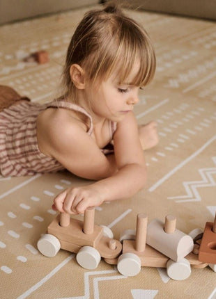 Kind speelt met houten trein op de OLYA KIDS Boho Zand speelmat in woonkamer.