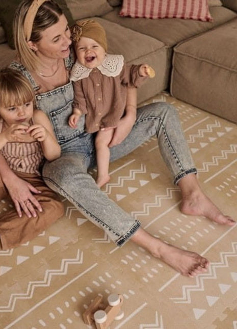Moeder zit met twee kinderen op de OLYA KIDS Boho Zand speelmat voor beige bank.