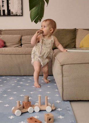 Baby staat bij bank op de OLYA KIDS Cross Azure speelmat met houten speelgoedtrein.