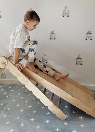 Kleuter speelt op houten glijbaan boven de OLYA KIDS Cross Azure speelmat in speelkamer.