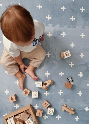 Bovenaanzicht van peuter zittend op de OLYA KIDS Cross Azure speelmat met houten blokken.