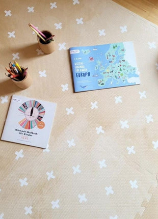 Detail van OLYA KIDS Cross Sand speelmat met boekjes en kleurpotloden erop.