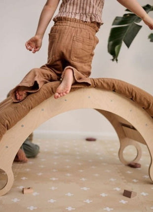 Kind klimt op een speelboog bovenop de OLYA KIDS Cross Sand schuimpuzzelmat.