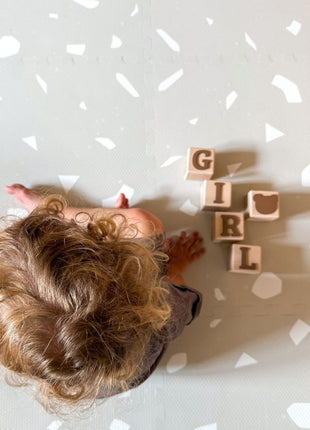 Bovenaanzicht van kleuter op de OLYA KIDS Terrazzo Dove speelmat met houten blokken.