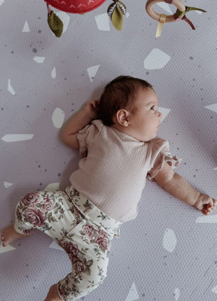 Baby onder speelboog op de OLYA KIDS Terrazzo Lavendel speelmat met terrazzo-patroon.