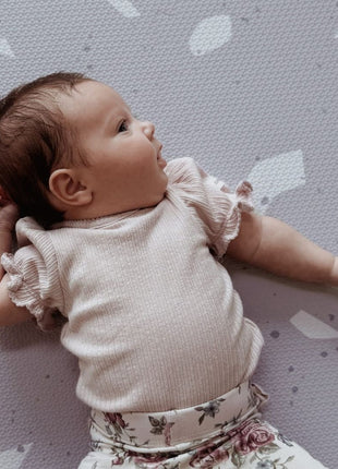 Baby kijkt op de zij op de OLYA KIDS Terrazzo Lavendel speelmat met terrazzo-patroon.