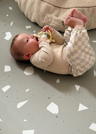 Baby ligt op de OLYA KIDS Terrazzo Sage speelmat en houdt een speeltje vast.