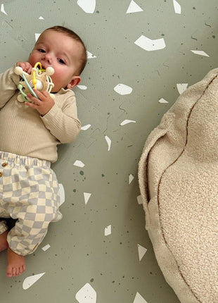 Baby ligt op de OLYA KIDS Terrazzo Sage speelmat met een pluche kussen ernaast.