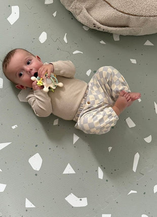 aby op de OLYA KIDS Terrazzo Sage speelmat naast een pluche kussen, van bovenaf gezien.