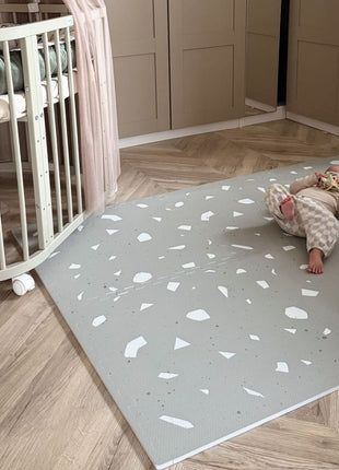 OLYA KIDS Terrazzo Sage speelmat met baby en wieg in slaapkamer met houten vloer.