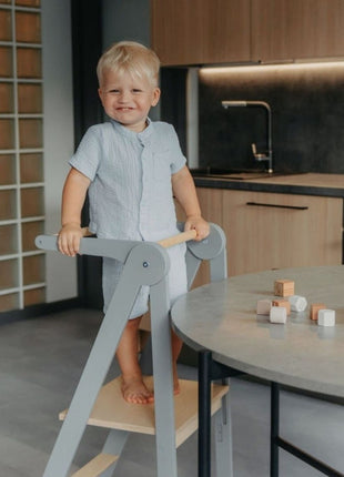 Kind staat op grijze Leg&Go opvouwbare keukentoren met verwijderbare rail bij ronde tafel.