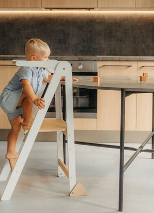 Kind klimt op witte Leg&Go opvouwbare keukentoren met verwijderbare rail naast tafel.