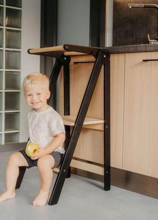 Kind zit op zwarte Leg&Go opvouwbare keukentoren met verwijderbare rail in keuken.