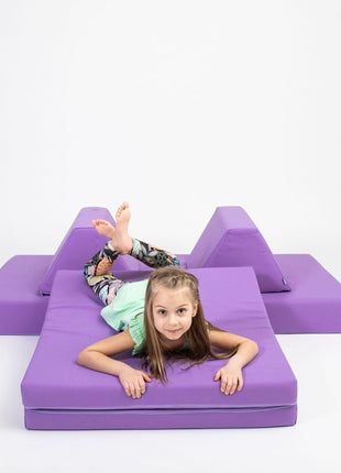 Kind speelt op het matras van de paarse Monboxy Montessori speelbank omringd door kussens – perfect voor zelfstandig en veilig spel.