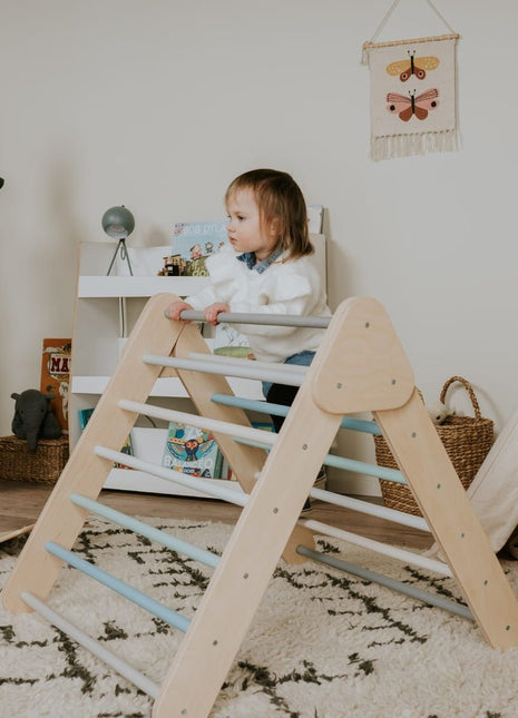 Pikler-driehoek – Pastel van leg&go met kind dat binnenshuis op de houten spijlen klimt.