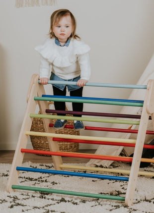 Pikler-driehoek - Regenboog van leg&go met kind dat op de houten spijlen staat.