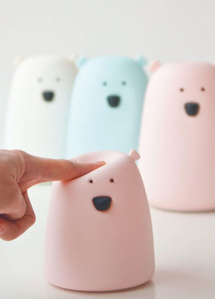Vinger drukt op Rabbit & Friends Nachtlampje Kleine Beer Roze met andere lampjes op achtergrond.