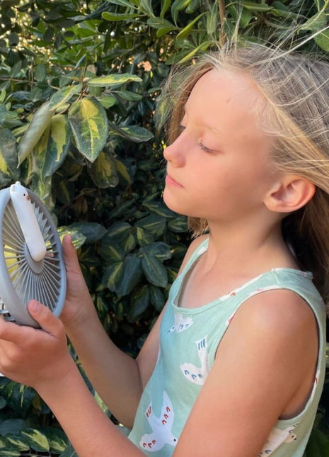 Meisje houdt Rabbit & Friends Ventilator met Nachtlicht grijs vast buiten bij struiken.