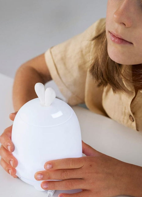 Kind houdt Rabbit & Friends Diffuser Lamp met konijnenoren vast op tafel.