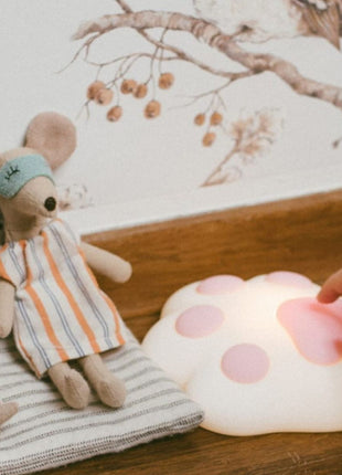 Rabbit & Friends Paw Nachtlampje verlicht op vloer met speelgoed en hand die lamp aanraakt.