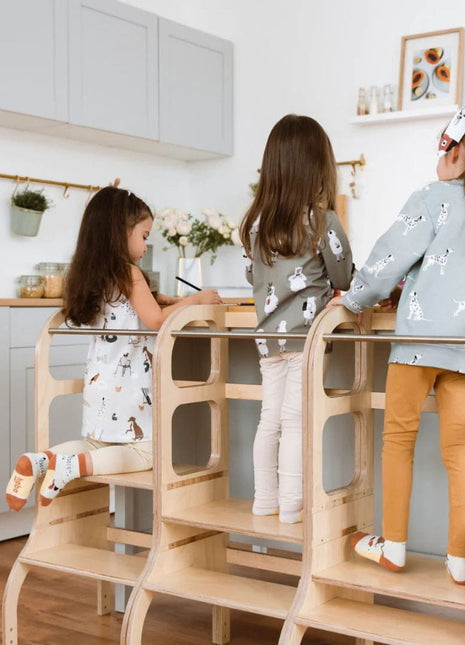 Drie meisjes staan op drie naturel STEP UP keukentorens en spelen samen aan keukenblad