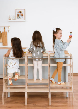 Drie kinderen staan naast elkaar op drie naturel STEP UP keukentorens met steunpoten aan keukeneiland