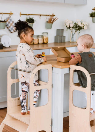 Twee jonge kinderen gebruiken naturel STEP UP keukentorens met steunpoten aan keukenblad.