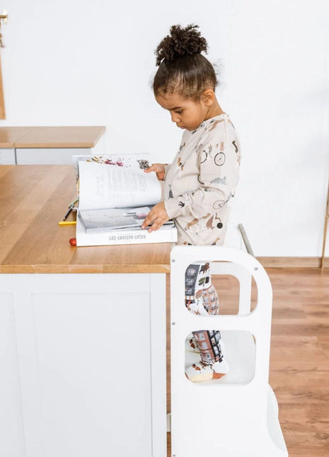 Meisje staat op witte STEP UP keukentoren met steunpoten en bladert in open boek aan keukeneiland