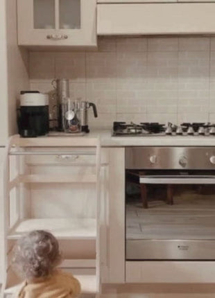 Peuter zit op de vloer voor witte STEP UP keukentoren met steunpoten bij keuken met oven