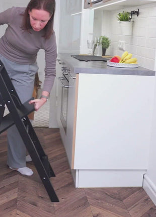 Volwassene klapt de STEP'n'FOLD opvouwbare keukentoren zwart in naast het aanrecht in de keuken