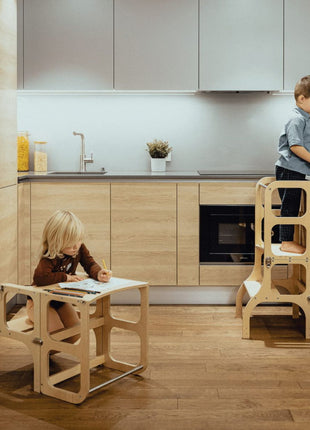 Eén kind staat aan het aanrecht in de STEP'n'SIT® 2-in-1 keukentoren naturel terwijl ander kind tekent aan tafelstand