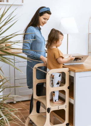 Kind staat aan het keukeneiland in de STEP'n'SIT® 2-in-1 keukentoren naturel terwijl ouder toekijkt