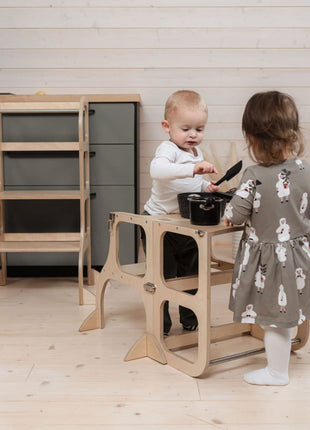 Twee kinderen gebruiken de STEP'n'SIT® 2-in-1 keukentoren naturel met steunpoten als tafel met kookspel