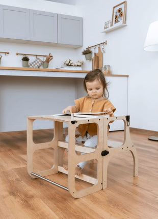 Peuter zit aan de STEP'n'SIT® 2-in-1 keukentoren naturel in tafelstand en bekijkt een boek