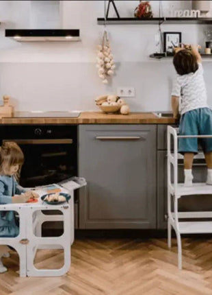 Eén kind staat aan het aanrecht in de STEP'n'SIT® 2-in-1 keukentoren wit terwijl ander kind tafelstand gebruikt